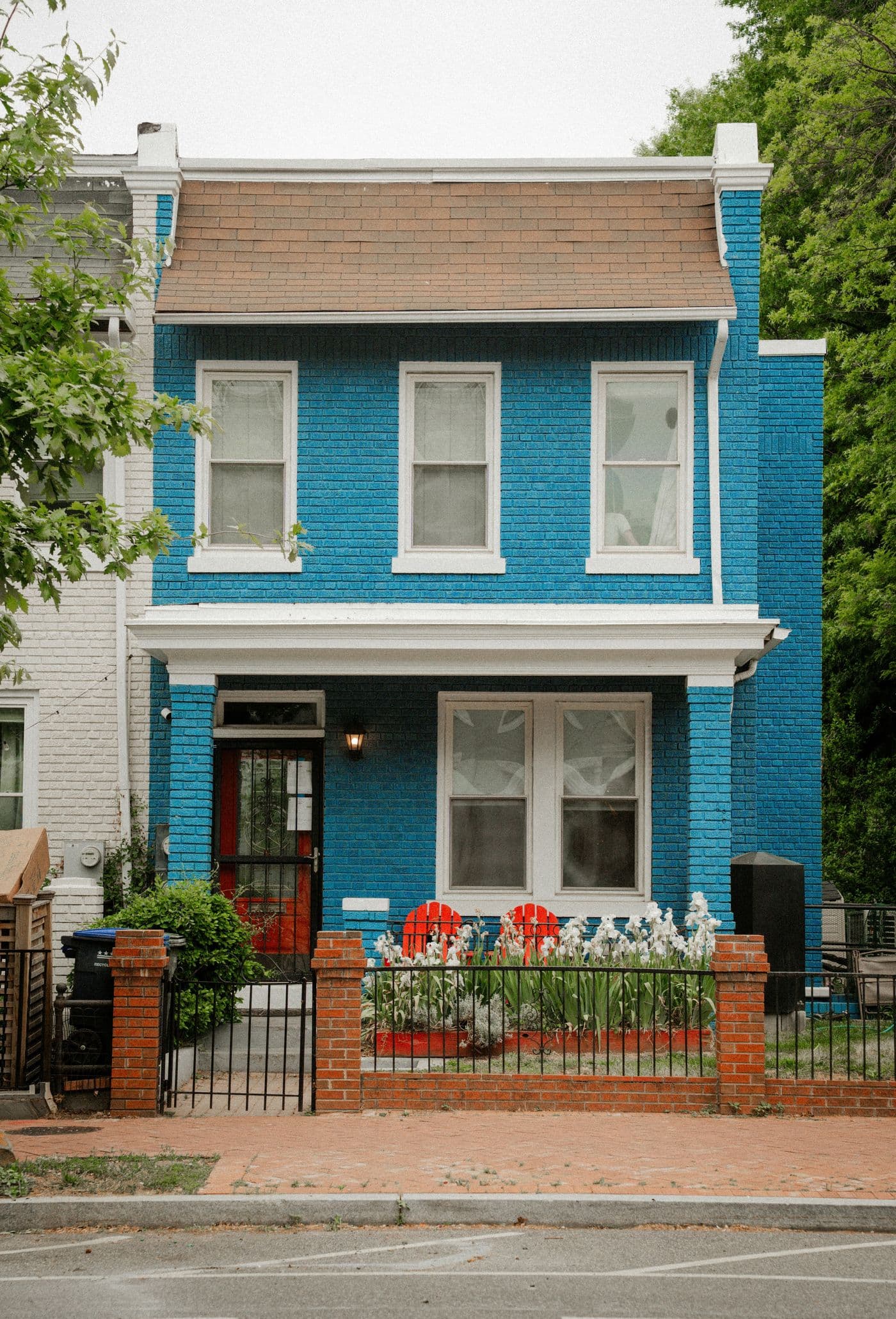 A blue-painted brick porch-front rowhouse with a red front door and spring flowers in Washington, DC
